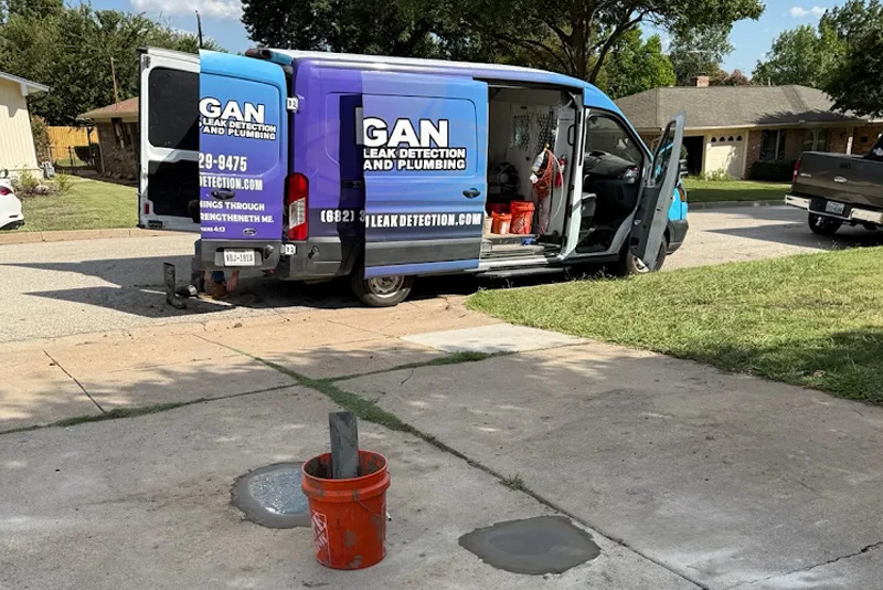 Two patched concrete areas in a residential driveway after slab leak reroute completed by Morgan Leak Detection & Plumbing service van in DFW.