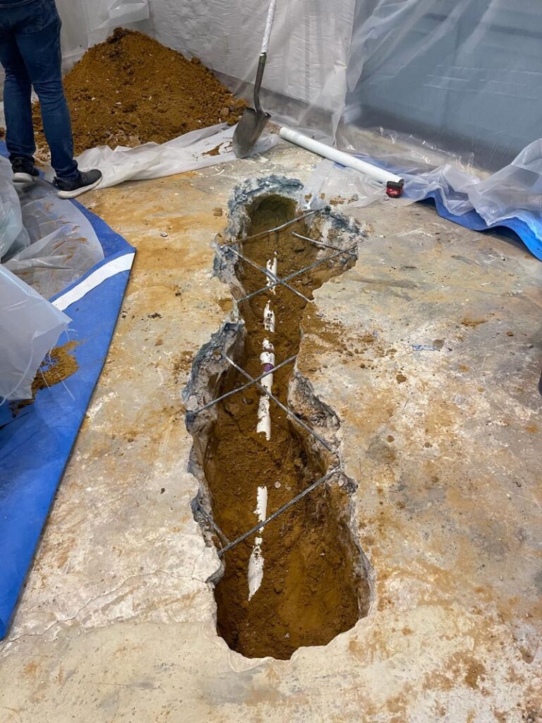 Trench in concrete slab exposing PVC line during slab leak repair, dust containment and debris control in a Fort Worth home.